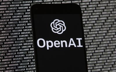 Логотип OpenAI появляется на экране мобильного телефона перед экраном компьютера со случайными двоичными данными